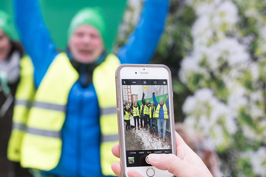 En grupp av John Mattsons medarbetare klädda i varselvästar poserar med uppsträckta armar för en fotografering framför en byggarbetsplats.