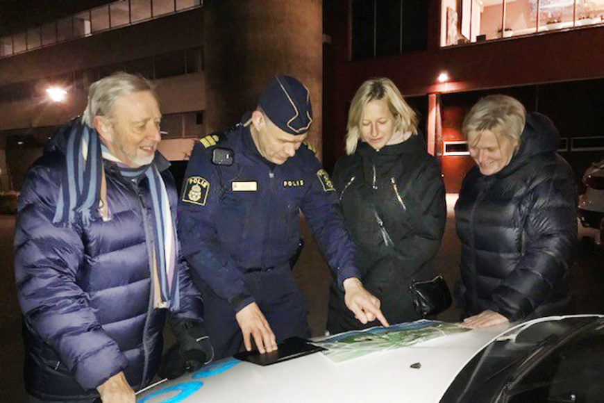 Fyra personer står utomhus och tittar på en karta som ligger på motorhuven till en polisbil.