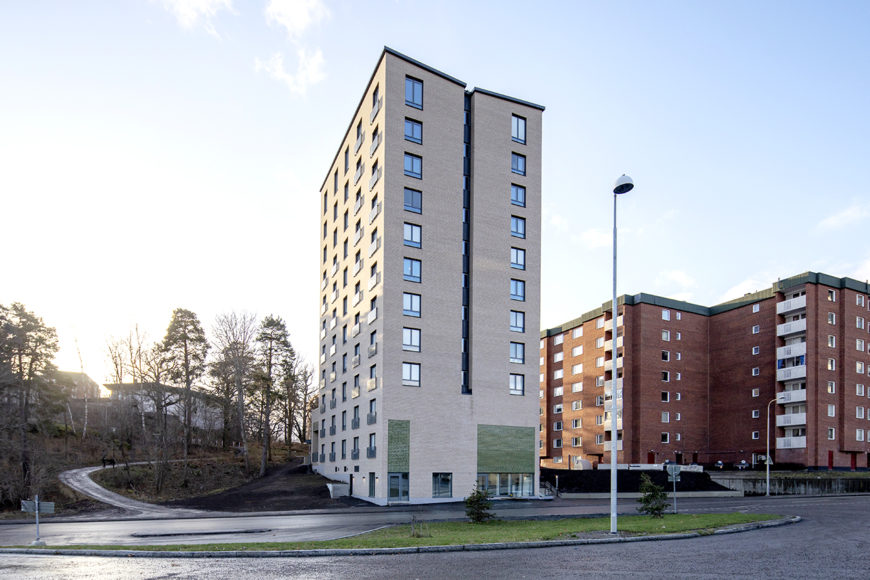 Nybyggd höghus med ljus tegelfasad framför äldre och mörkare tegelhus.