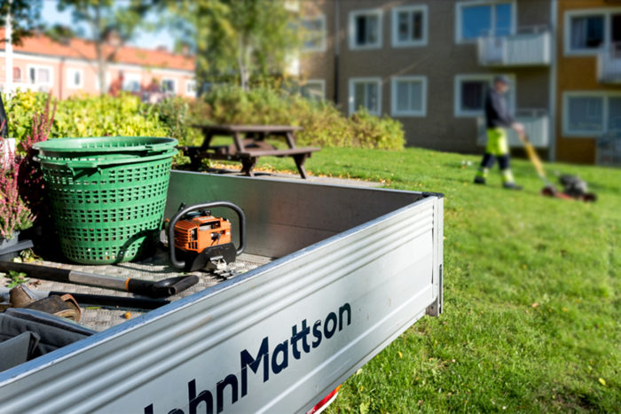 Man klipper gräs utanför ett flerfamiljshus.