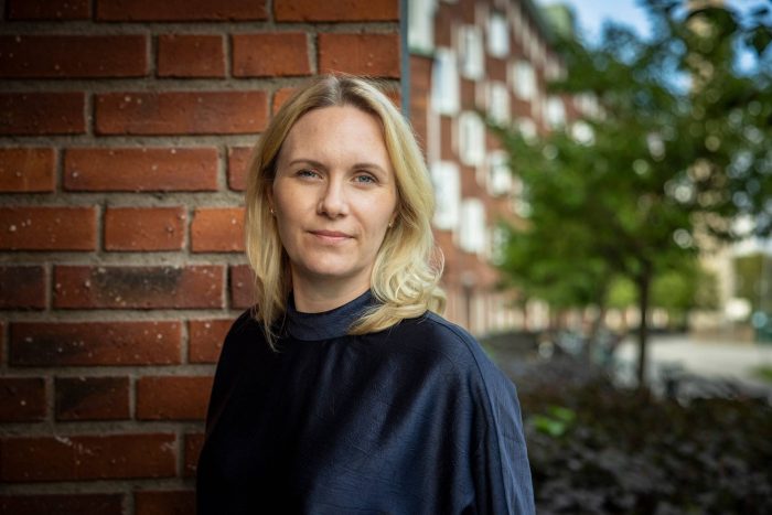 Louise Wall, hållbarhetschef på John Mattson, står utomhus framför en tegelvägg.