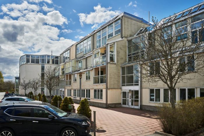 Flerbostadshus i Sollentuna med ljus fasad, inglasade balkonger och parkerade bilar framför entrén
